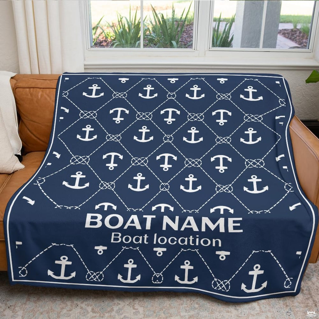 Navy nautical anchor graphic throw blanket draped neatly across brown leather couch near bright window.