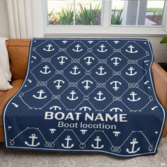 Navy nautical anchor graphic throw blanket draped neatly across brown leather couch near bright window.