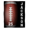 Flat view of football blanket displaying giant textured brown ball, white laces, and black athletic side panel
