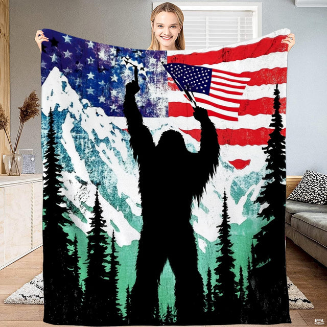 Woman holding up patriotic Bigfoot blanket displaying American flag over mountain peaks