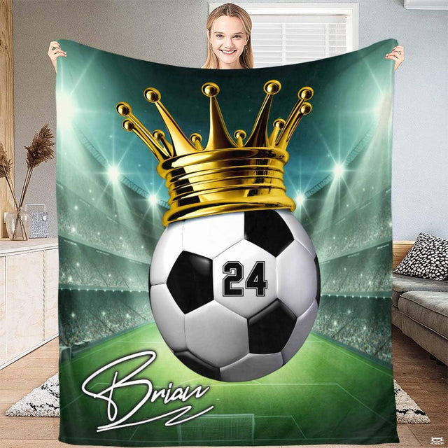 Full view of soccer ball crowned with golden tiara on glowing green stadium field on a sports blanket.