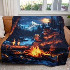 Folded Bigfoot campfire mountain throw blanket resting on wooden table displaying wilderness artwork