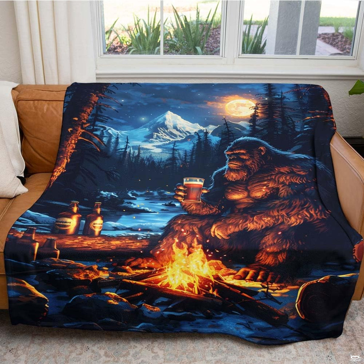 Folded Bigfoot campfire mountain throw blanket resting on wooden table displaying wilderness artwork