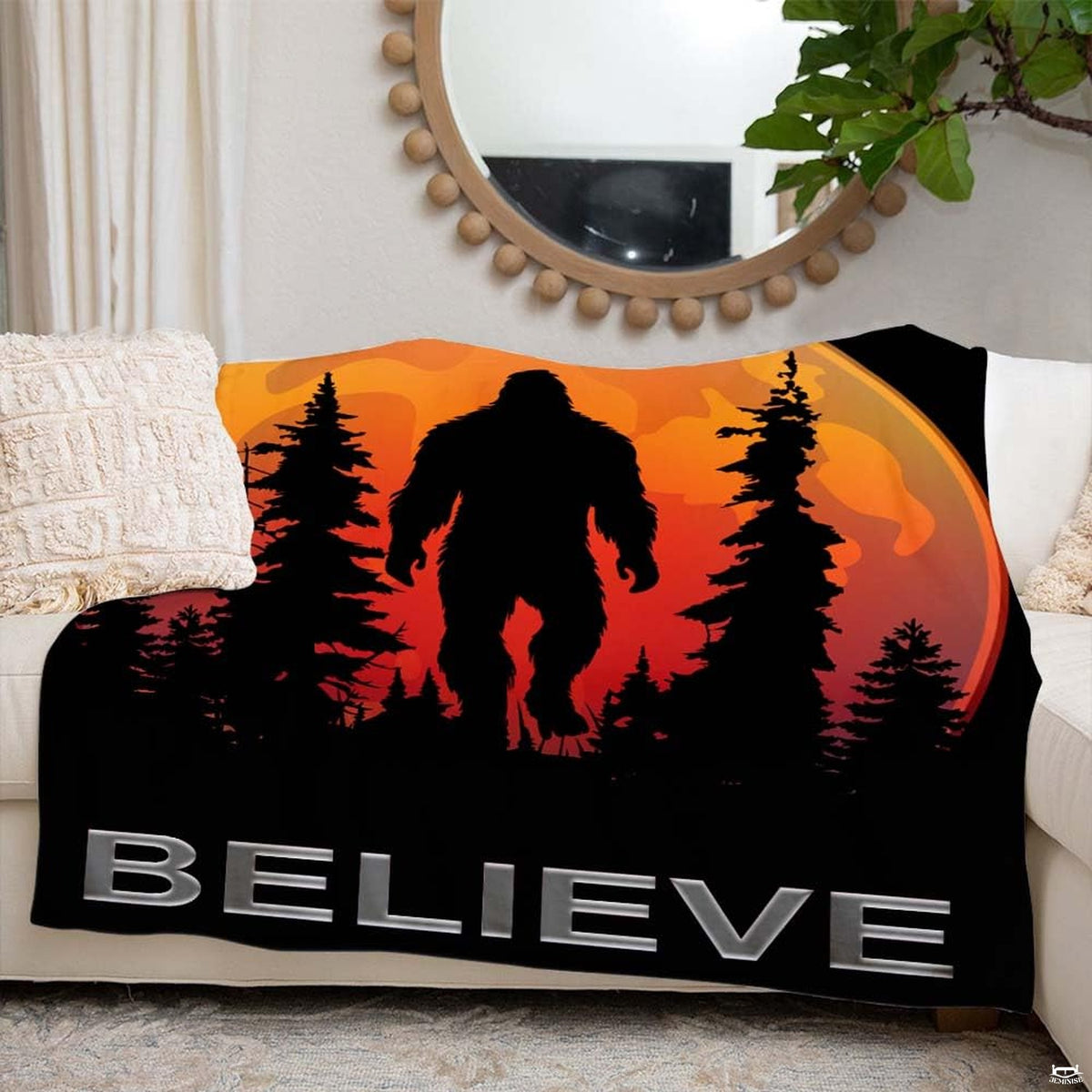 Sasquatch graphic throw blanket displayed neatly over white living room couch beneath round mirror.