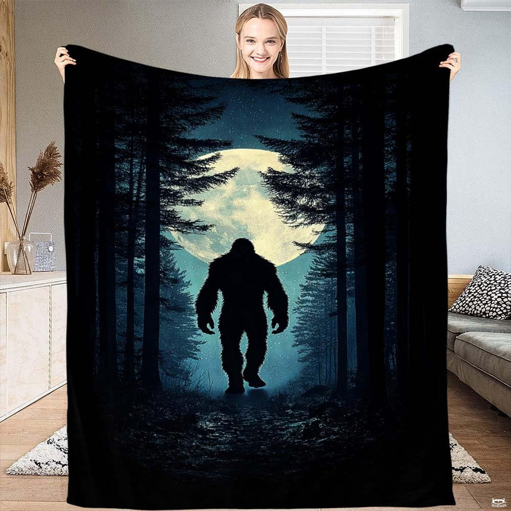 Woman holding up the nocturnal blanket displaying Bigfoot walking through a pine forest before a glowing moon.