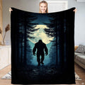 Woman holding up the nocturnal blanket displaying Bigfoot walking through a pine forest before a glowing moon.