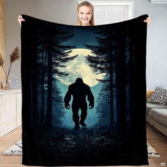 Woman holding up the nocturnal blanket displaying Bigfoot walking through a pine forest before a glowing moon.