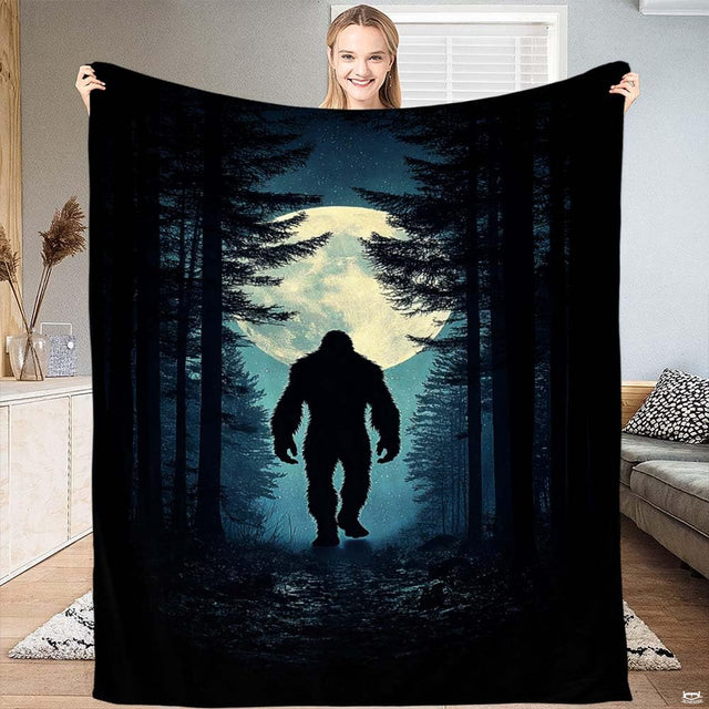 Woman holding up the nocturnal blanket displaying Bigfoot walking through a pine forest before a glowing moon.