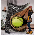 Softball in glove throw blanket held upright outdoors showing lime ball and brown fielder mitt.