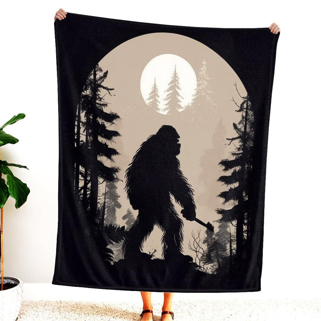 Person holding up the blanket displaying the Bigfoot silhouette walking in a pine forest under a glowing moon.