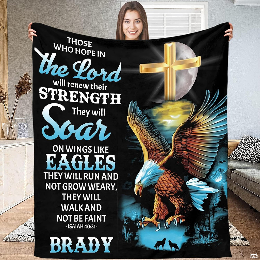 Person standing indoors holding up a decorative Christian cross and flying raptor throw blanket.