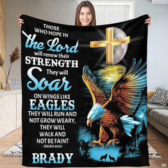 Person standing indoors holding up a decorative Christian cross and flying raptor throw blanket.