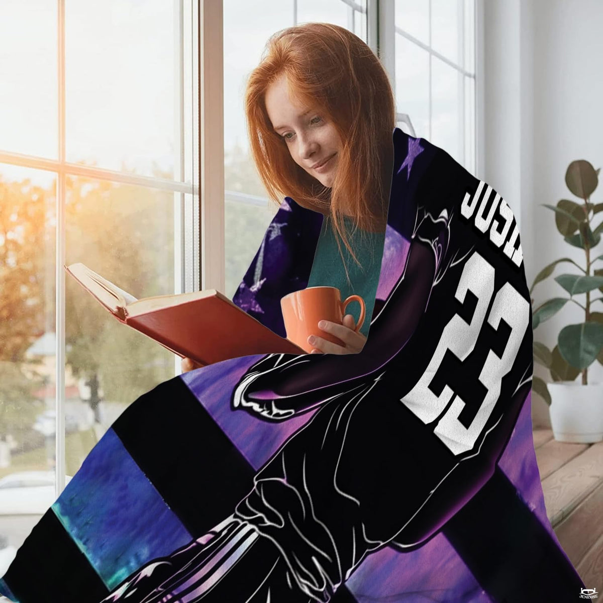 Person relaxing beside window reading with beverage draped in the galaxy football print.