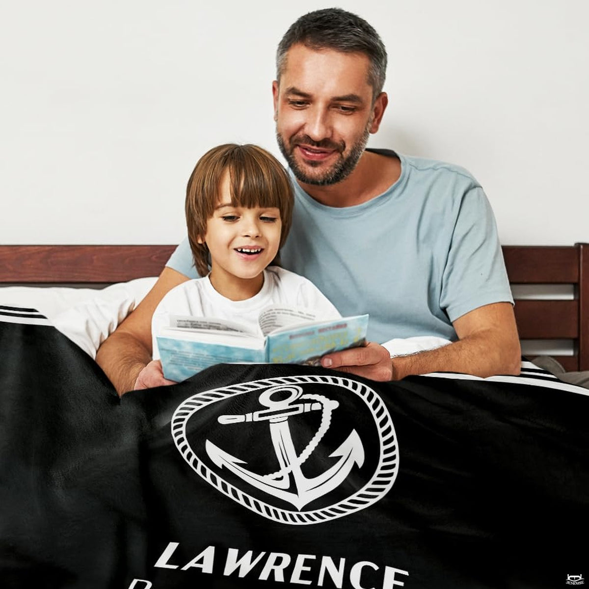 Parent and child reading a book in bed draped in the nautical anchor print.