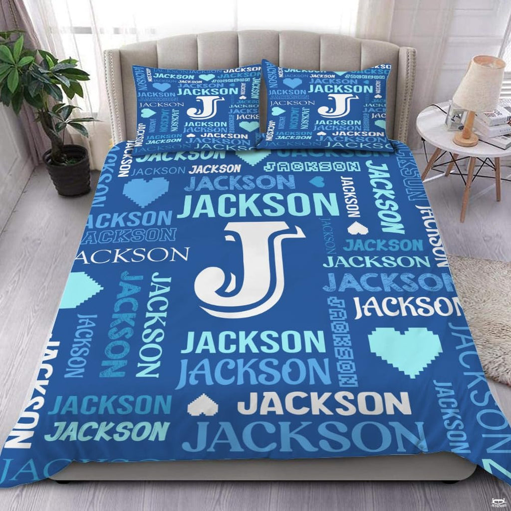 Close-up view of bedding detailing bold initial outline, pixel heart motifs, and vibrant blue typography accents