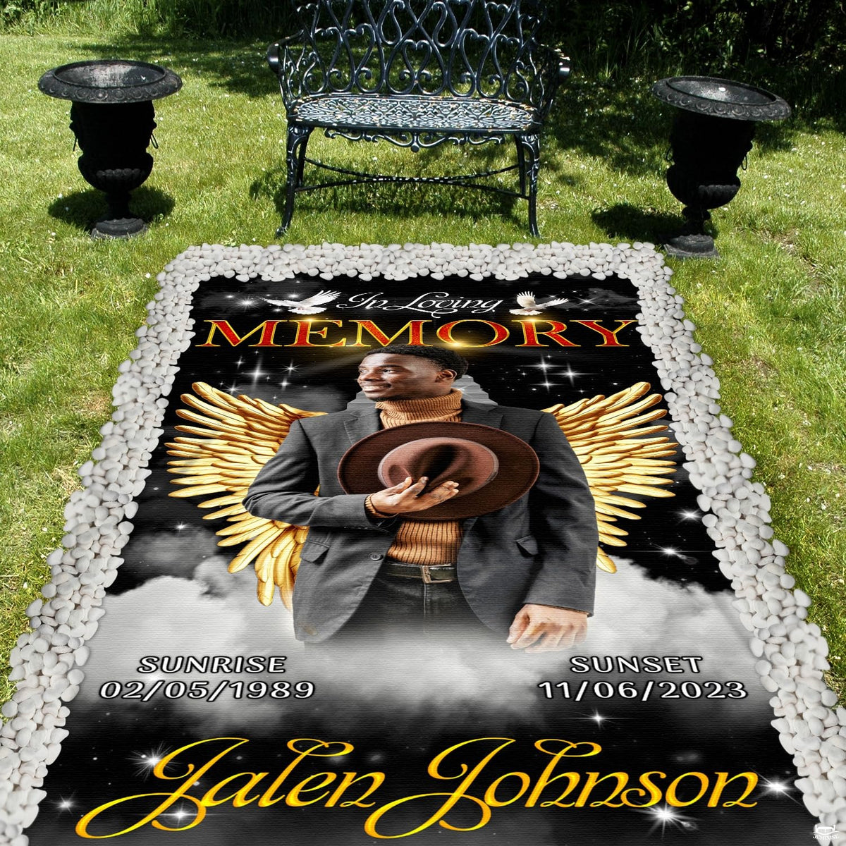 Cemetery lawn memorial setting showcasing the angel wings tribute blanket with decorative stone border.