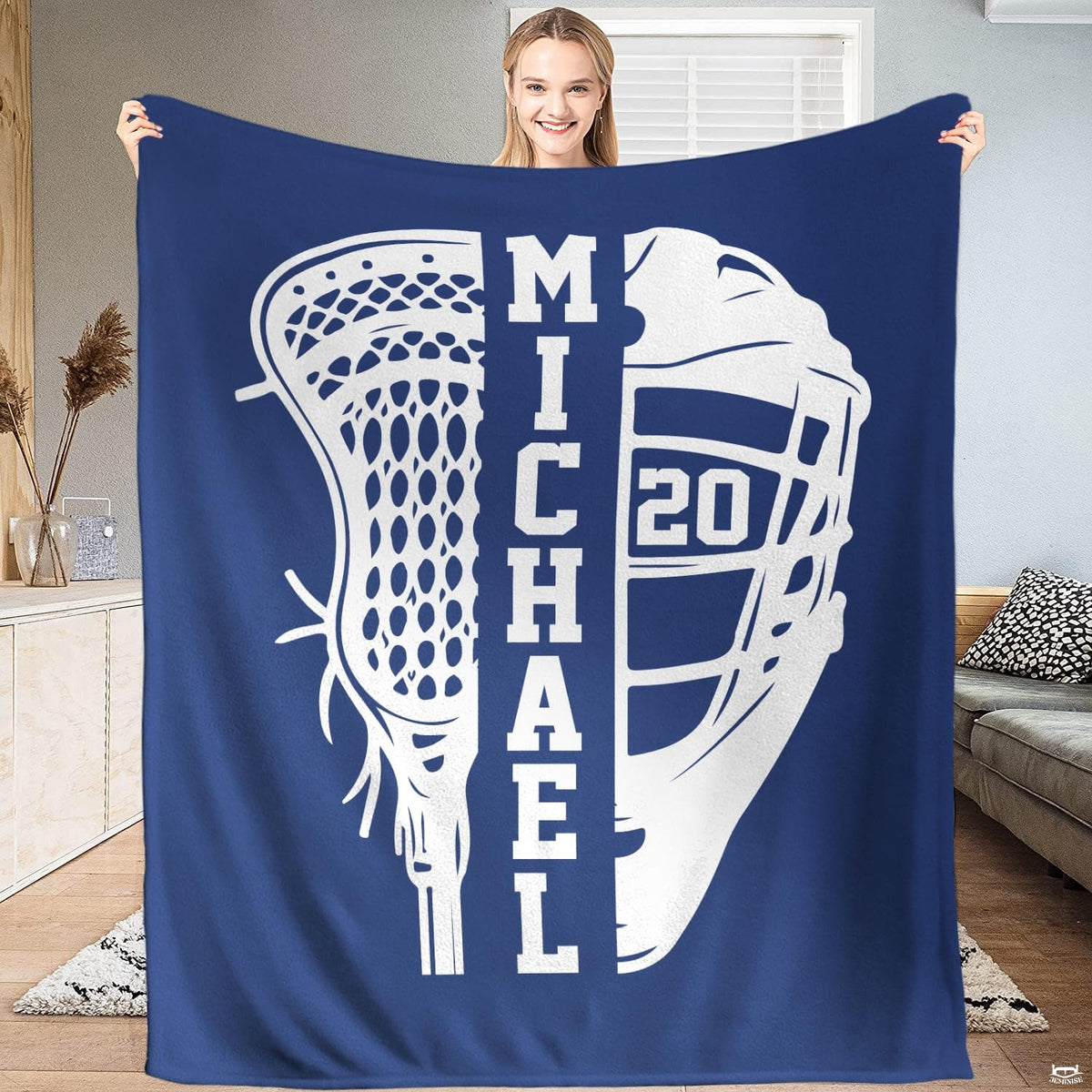 Person standing indoors holding up a sapphire lacrosse stick and helmet sports blanket.