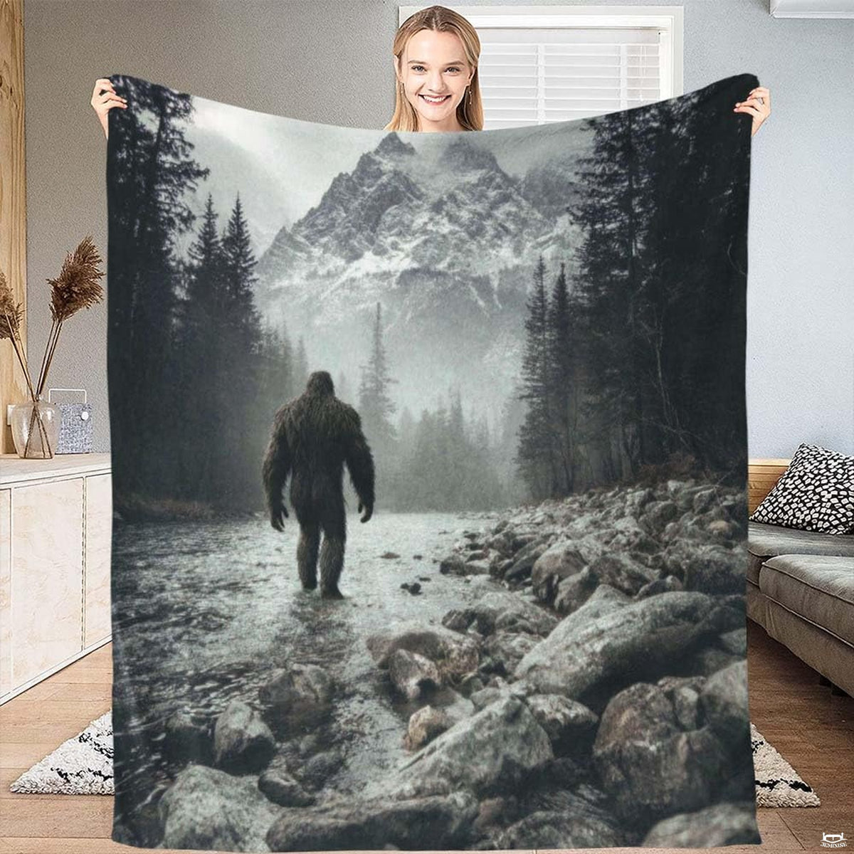 Bigfoot walking through a rocky mountain river toward snow-capped peaks, view 1.