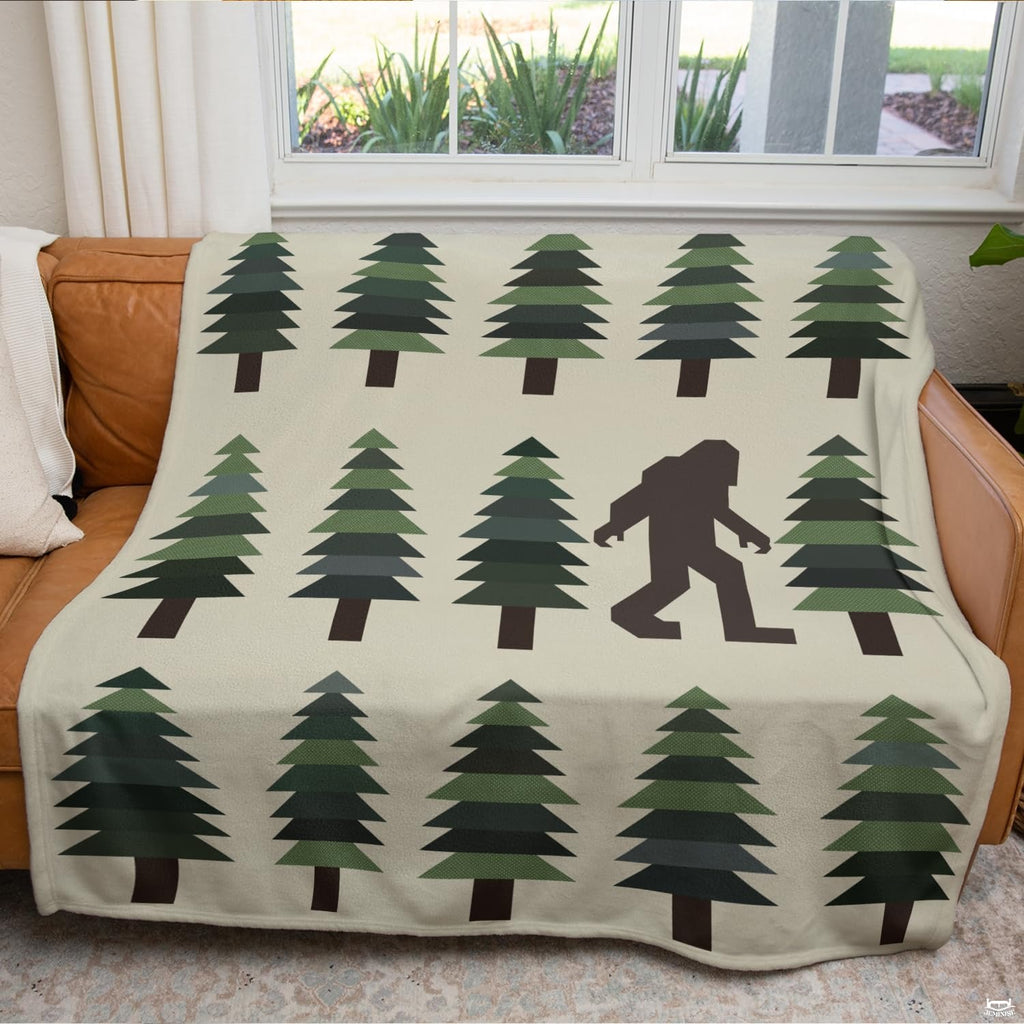 Folded blanket showing geometric evergreen pine tree rows and Bigfoot motif on cream background.