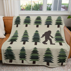 Folded blanket showing geometric evergreen pine tree rows and Bigfoot motif on cream background.
