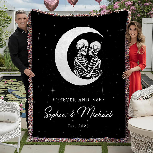 Couple holding gothic skeleton lovers throw blanket featuring crescent moon artwork and colorful fringed trim