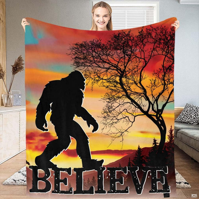 Woman holding up Bigfoot sunset blanket featuring Sasquatch silhouette and bare tree