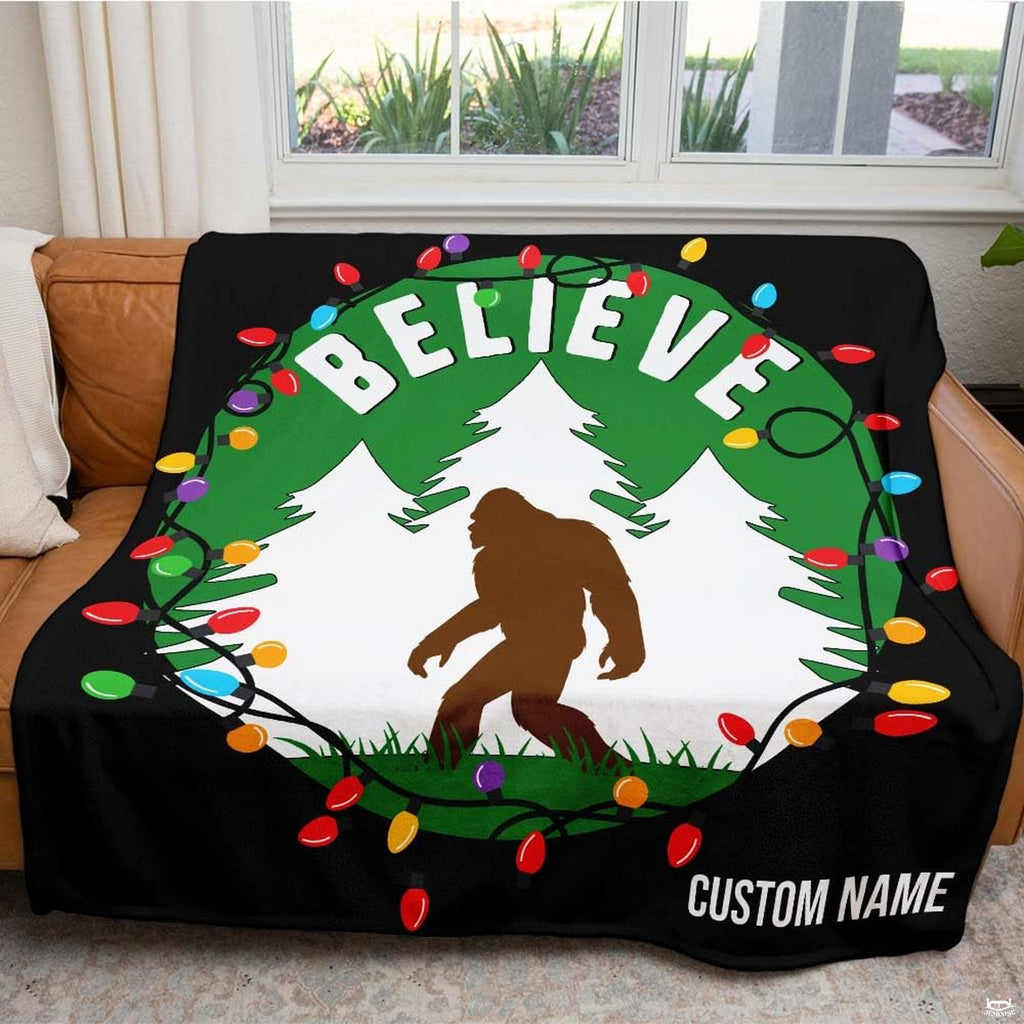 Brown Bigfoot walking in snowy forest framed by Christmas lights wreath and arched lettering, view 3.