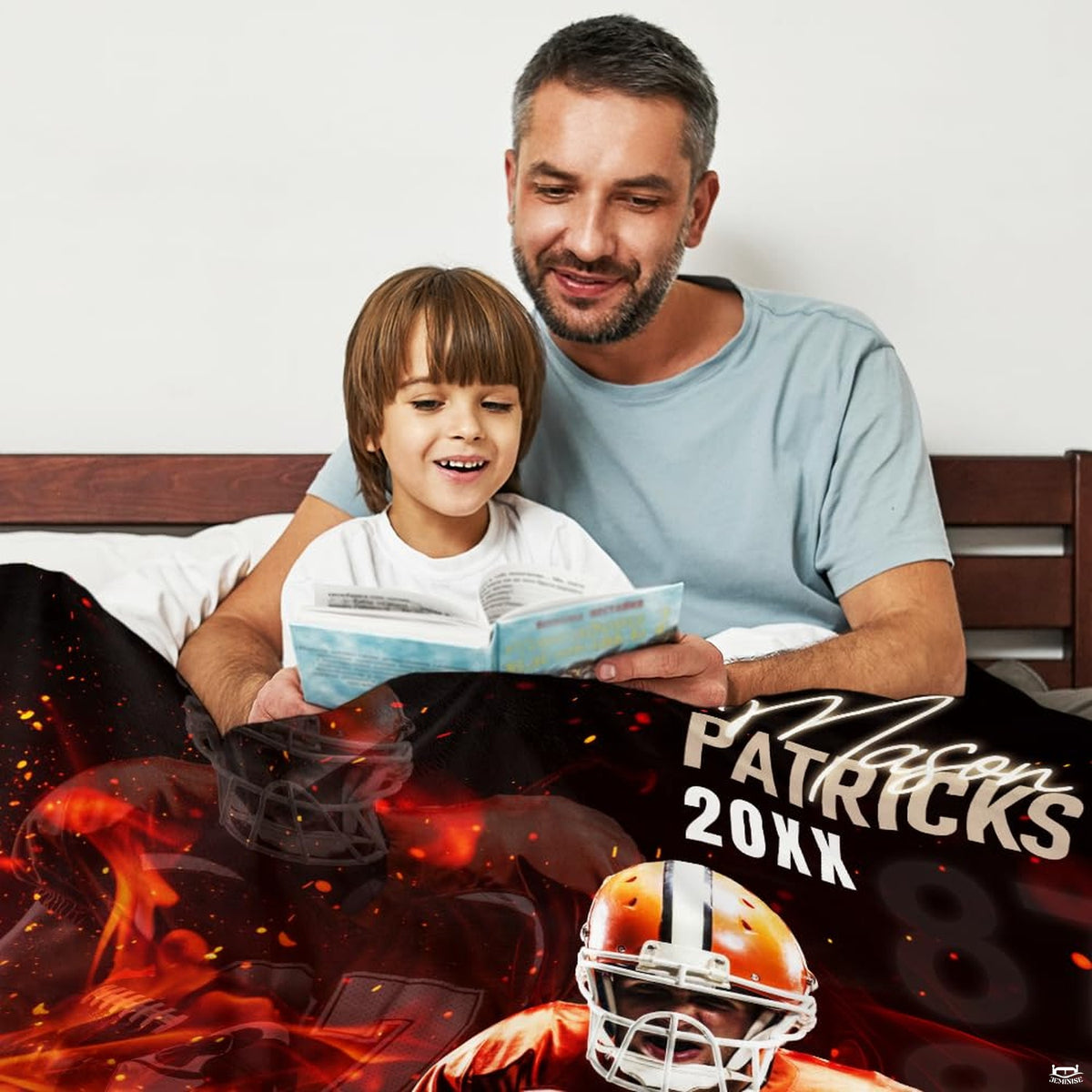 Father and child reading storybook in bed under fiery athletic football player graphic throw blanket.