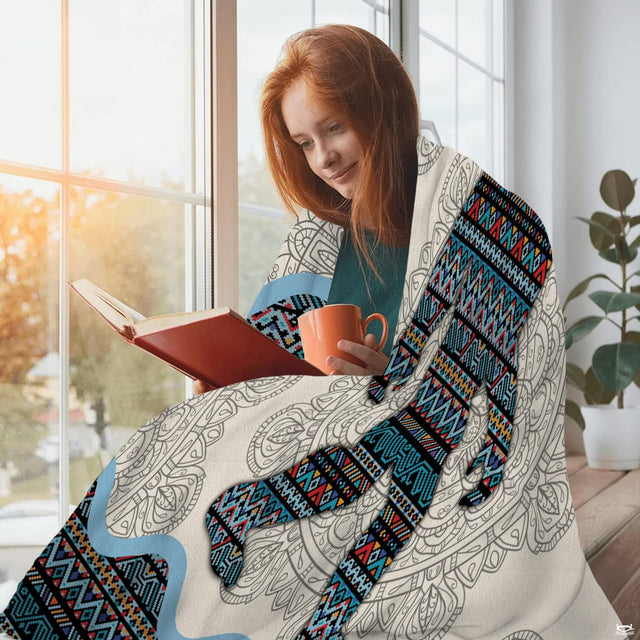Tribal Bigfoot throw blanket styled around a person reading by a window with a warm drink.