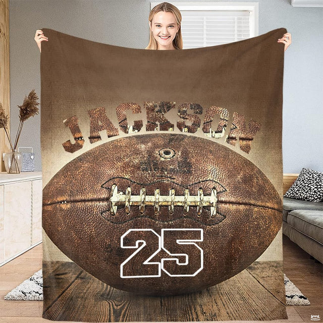 Woman holding up vintage football throw blanket displaying rustic ball graphics and collegiate lettering