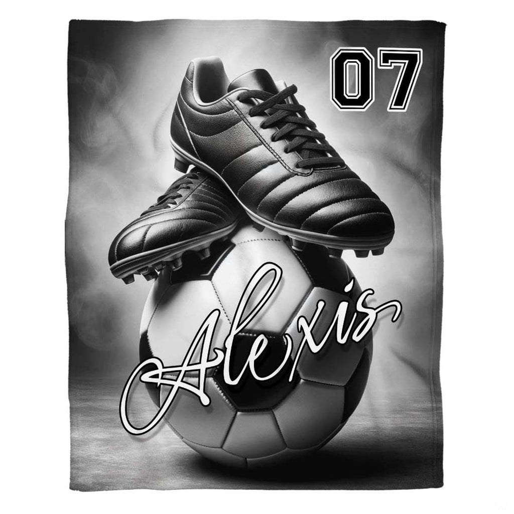 Monochrome soccer cleats atop a ball with bold jersey numerals and cursive script over a smoky backdrop.