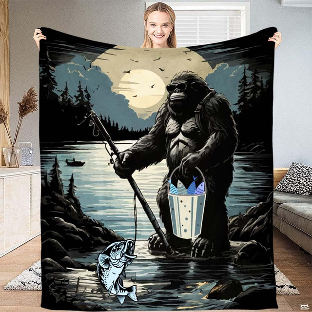 Woman holding up fishing Bigfoot graphic throw blanket showcasing lake landscape and moonlit mountain scene.