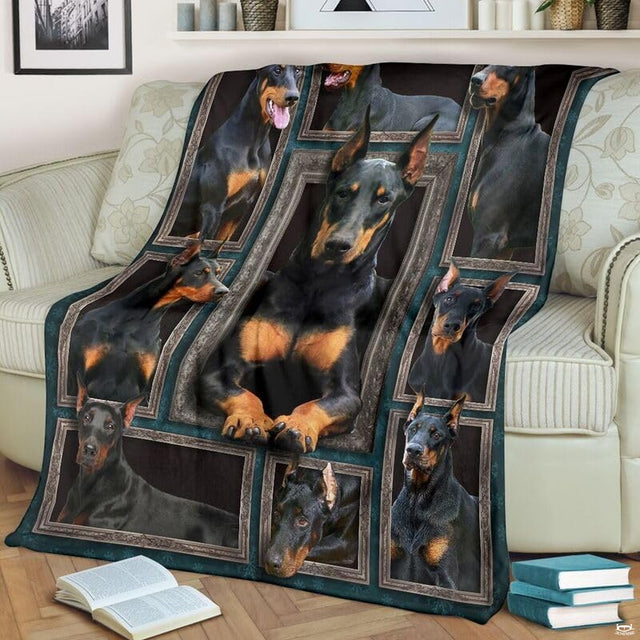 Doberman Pinscher throw blanket styled across a living room sofa near stacked books and a cup.