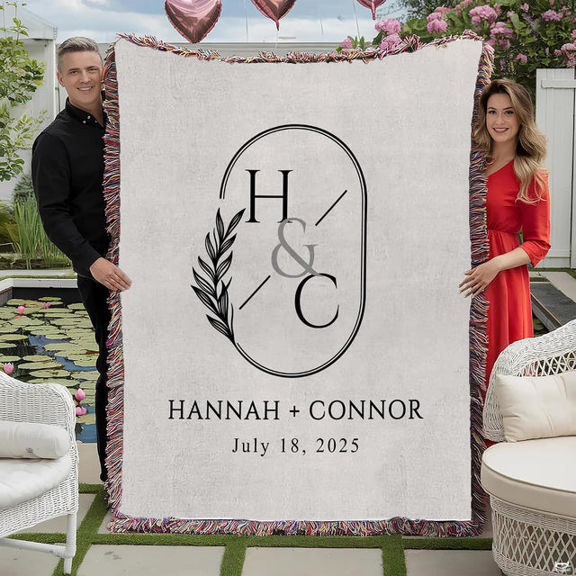 Couple holding modern oval crest wedding throw blanket with botanical olive branch and colorful fringe