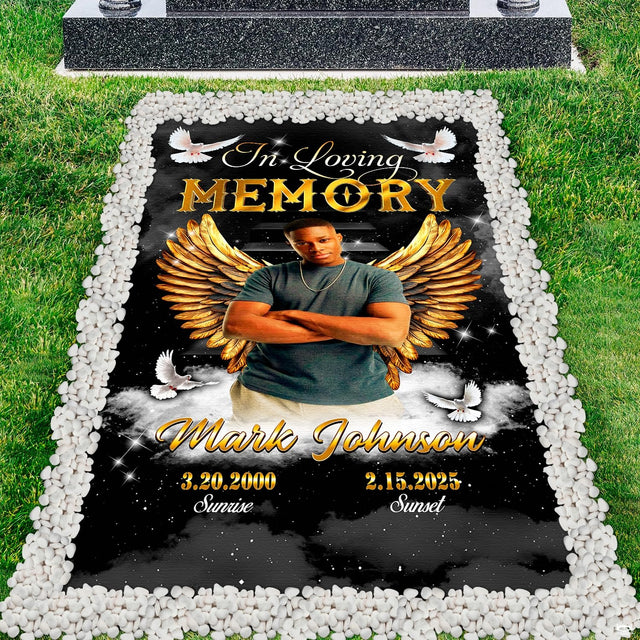 Top-down cemetery perspective showing celestial angel wings tribute placed before a polished headstone.