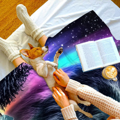 Overhead view of person and puppy resting on celestial star-filled northern lights pattern.