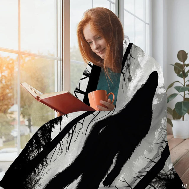 Person sitting beside a window with a mug and book while draped in the misty forest Bigfoot textile.