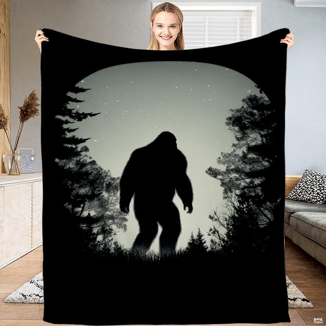 Woman holding up a black blanket displaying Bigfoot walking through a starry pine forest clearing.