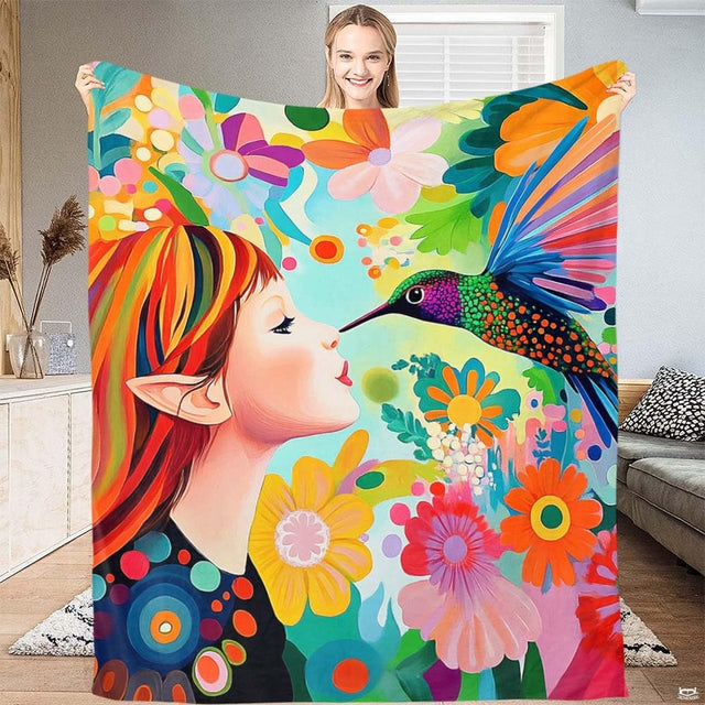 Woman holding up a blanket featuring a whimsical rainbow-haired fairy and a colorful hummingbird.