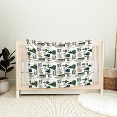 Close-up of watercolor spruce trees and antlered deer silhouettes on forest nursery bedding.