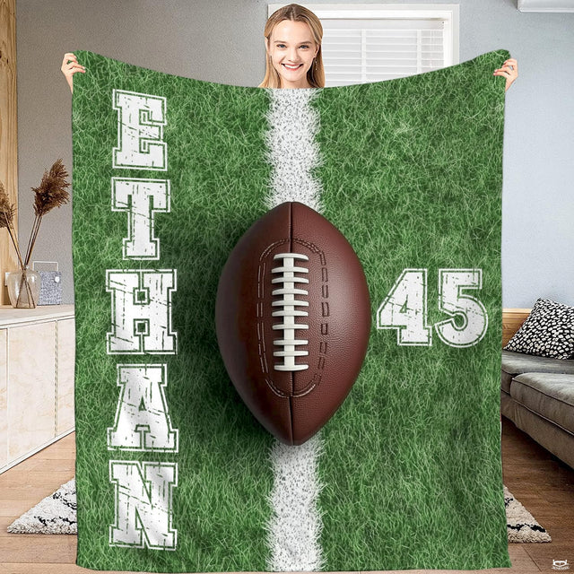 Football blanket held up displaying green turf background, yard chalk line, and central football graphic