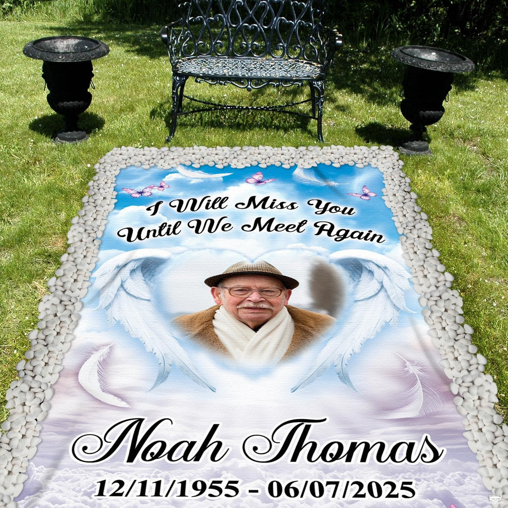 Outdoor cemetery display of memorial angel wings grave blanket laid on lawn surrounded by pebbles.