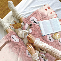 Top-down view of person relaxing under family tree blanket alongside pet dog and book