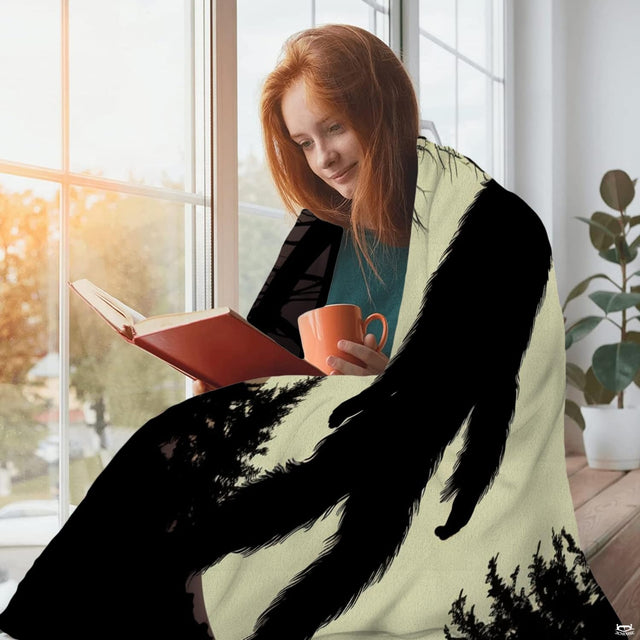 Woman sitting beside a window reading a book draped in the ivory moon Bigfoot print textile.