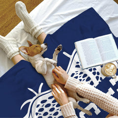 Puppy resting on a draped sapphire sports blanket beside an open book and beverage mug.