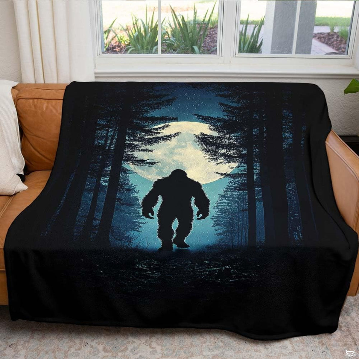 Nocturnal pine forest Bigfoot blanket draped over an indoor living room couch near a bright window.