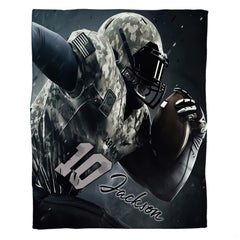 Flat view of camo football blanket displaying military uniform athlete charging forward on dark backdrop