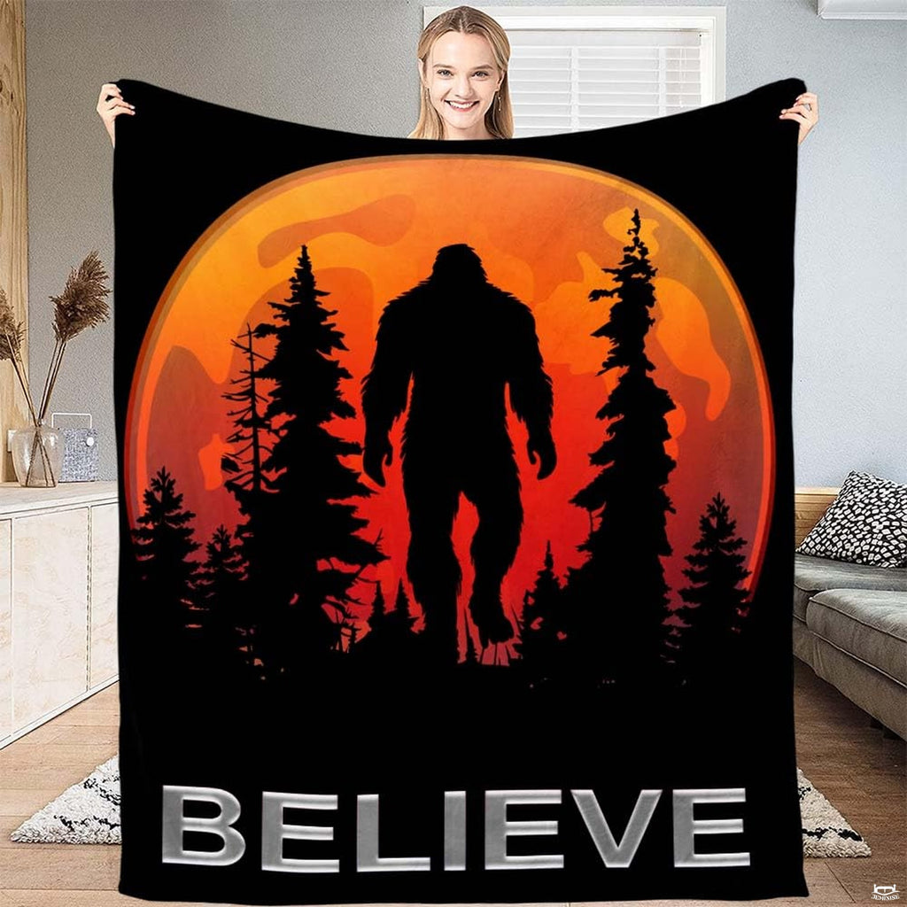 Woman displaying black Bigfoot graphic throw blanket with glowing orange harvest moon and pine forest.