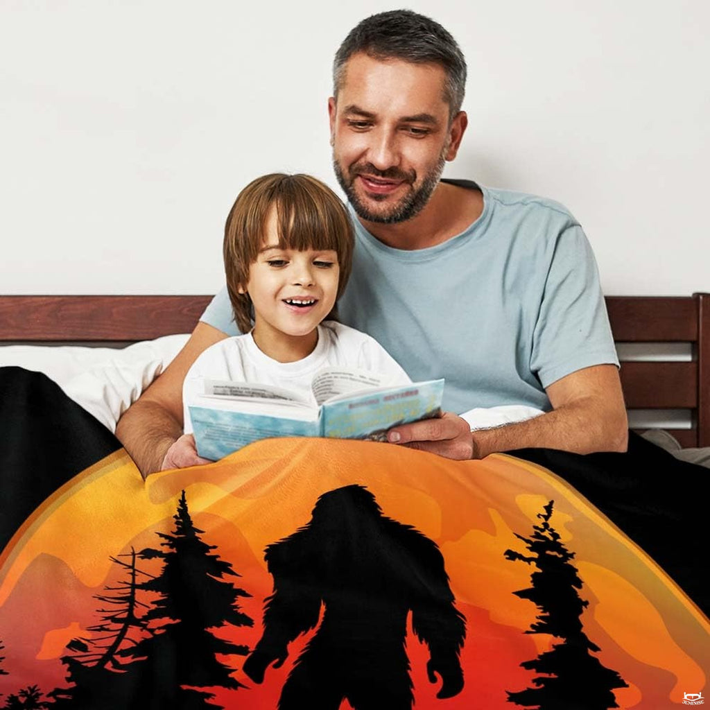 Father and son reading storybook together in bed under glowing full moon Bigfoot graphic throw blanket.