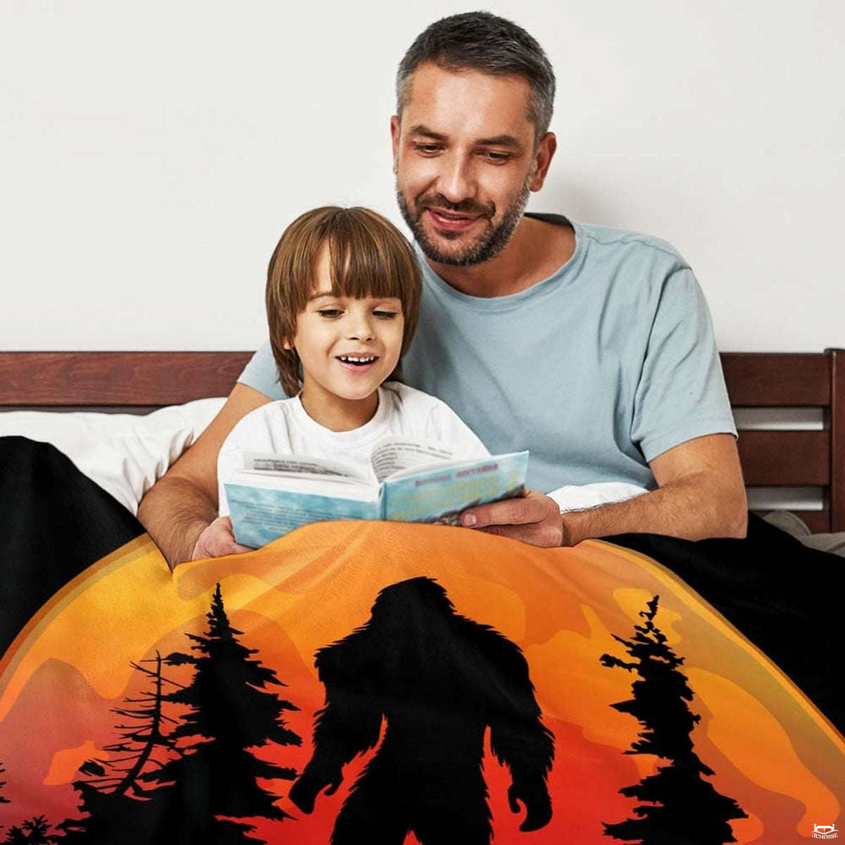 Father and son reading storybook together in bed under glowing full moon Bigfoot graphic throw blanket.